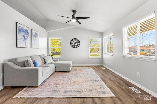 living area with ceiling fan, baseboards, healthy amount of natural light, wood finished floors, and vaulted ceiling