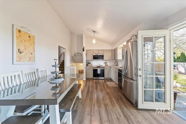 kitchen with appliances with stainless steel finishes, vaulted ceiling, wood finished floors, backsplash, and light countertops