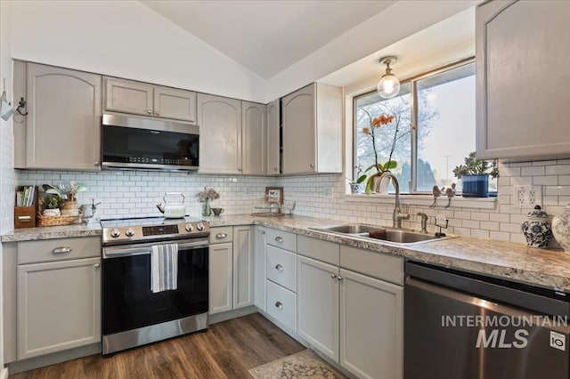 kitchen featuring appliances with stainless steel finishes, a sink, lofted ceiling, dark wood finished floors, and backsplash
