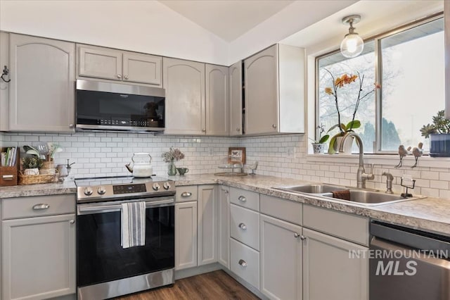 kitchen with appliances with stainless steel finishes, a sink, vaulted ceiling, light countertops, and dark wood-style floors