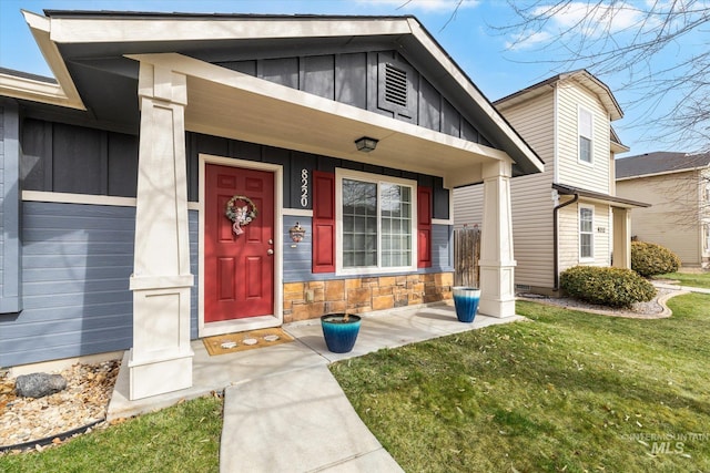 entrance to property featuring covered porch, stone siding, a lawn, and board and batten siding