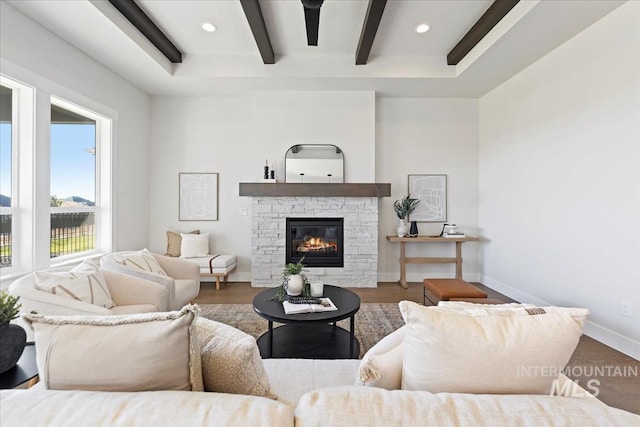 living room with beamed ceiling, baseboards, a stone fireplace, and wood finished floors