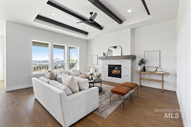 living area with wood finished floors, baseboards, ceiling fan, a stone fireplace, and beamed ceiling