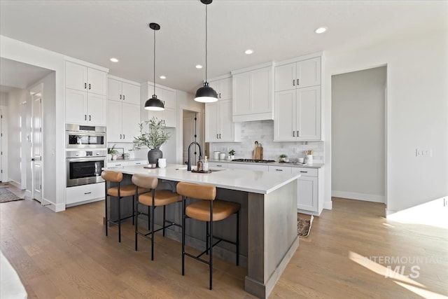 kitchen with an island with sink, stainless steel double oven, white cabinets, and a kitchen bar