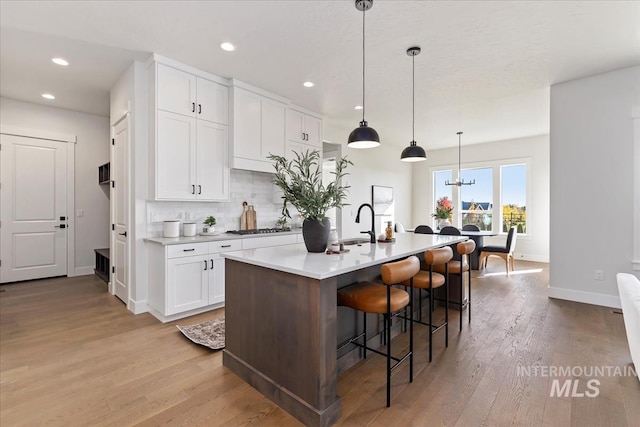 kitchen with a breakfast bar, light wood-style flooring, tasteful backsplash, white cabinetry, and gas stovetop