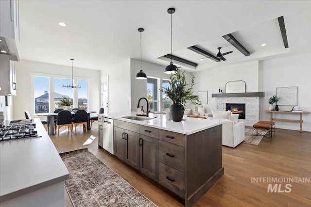 kitchen featuring a sink, dark brown cabinets, a stone fireplace, appliances with stainless steel finishes, and dark wood-style flooring