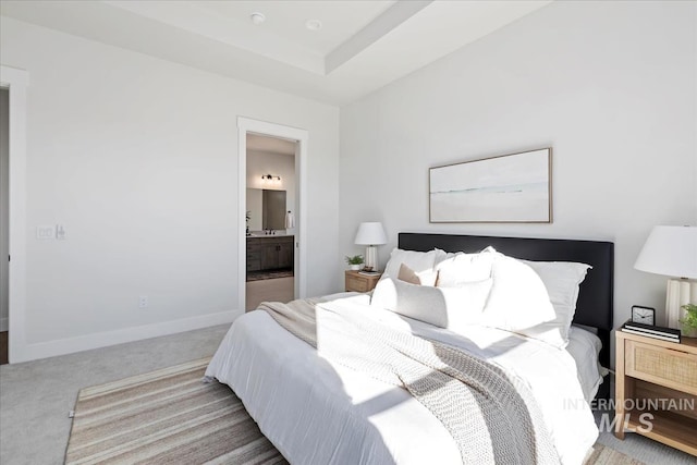 bedroom with a tray ceiling, baseboards, ensuite bathroom, and carpet