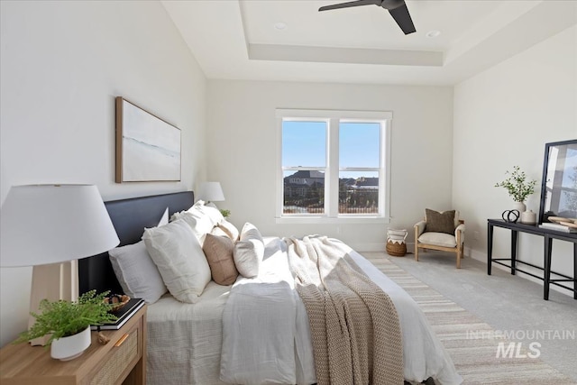 bedroom featuring light colored carpet, baseboards, a tray ceiling, and ceiling fan