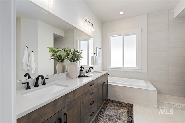 bathroom featuring double vanity, recessed lighting, a relaxing tiled tub, and a sink