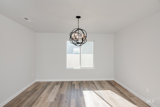 unfurnished room with visible vents, baseboards, an inviting chandelier, and wood finished floors