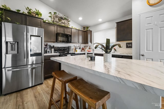 kitchen featuring light wood-type flooring, black appliances, a kitchen breakfast bar, lofted ceiling, and dark brown cabinets