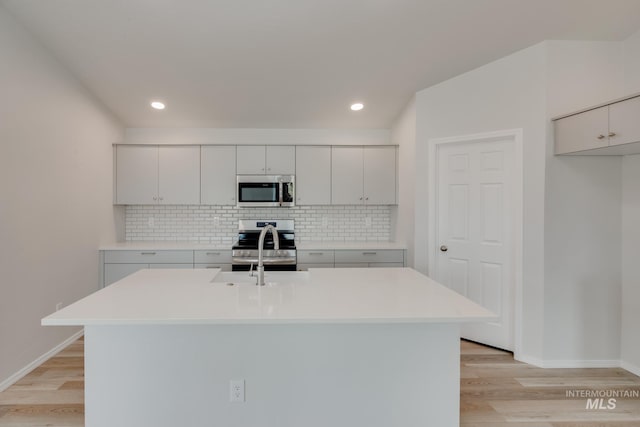 kitchen featuring light countertops, light wood finished floors, tasteful backsplash, and appliances with stainless steel finishes
