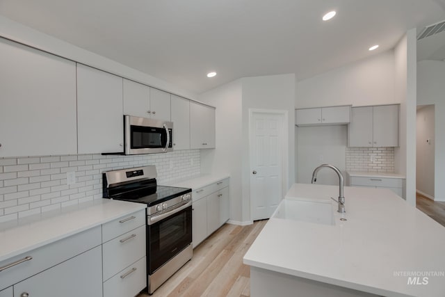 kitchen featuring light wood-style floors, stainless steel appliances, decorative backsplash, and a sink