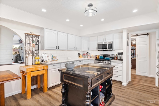 kitchen featuring white cabinetry, light stone countertops, a barn door, appliances with stainless steel finishes, and light wood-type flooring