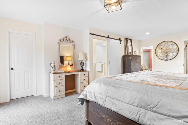 bedroom with ensuite bathroom, a barn door, and light carpet