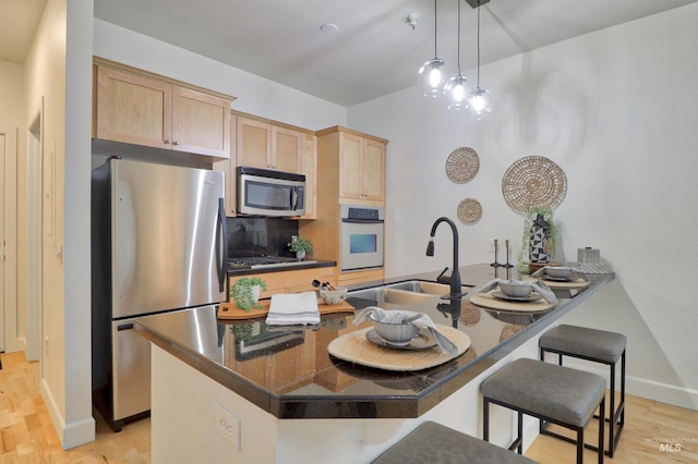 kitchen featuring sink, light hardwood / wood-style flooring, light brown cabinetry, a breakfast bar, and appliances with stainless steel finishes