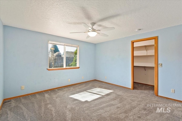 unfurnished bedroom featuring a textured ceiling, a closet, carpet, baseboards, and a spacious closet