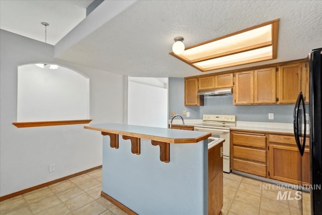 kitchen with freestanding refrigerator, light countertops, under cabinet range hood, a kitchen breakfast bar, and white range with electric stovetop