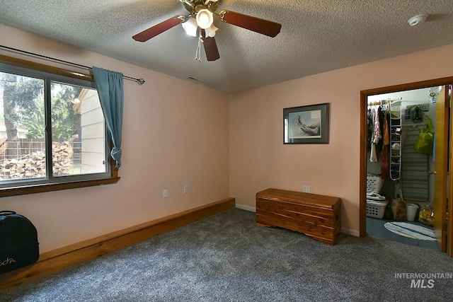 unfurnished bedroom featuring a spacious closet, a textured ceiling, and dark colored carpet