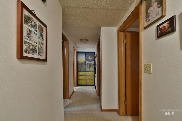 corridor with light colored carpet and a textured ceiling