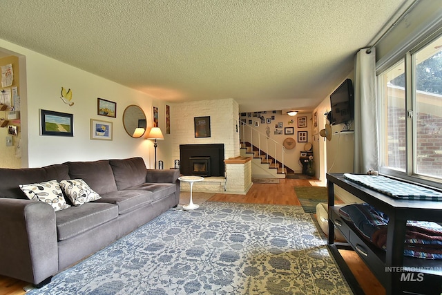 living room featuring wood-type flooring, a large fireplace, and a textured ceiling