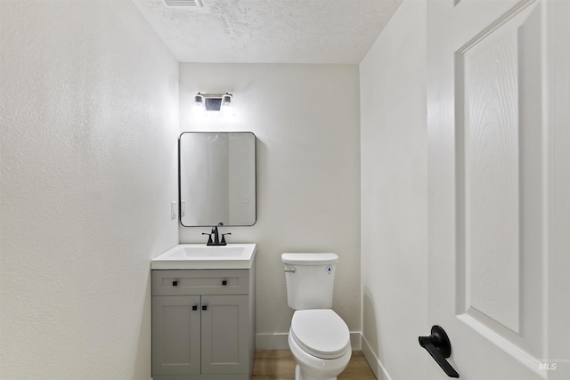 half bathroom with baseboards, toilet, wood finished floors, a textured ceiling, and vanity