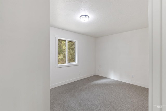 empty room with carpet floors, baseboards, and a textured ceiling