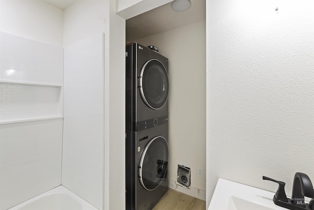 laundry area with light wood-style floors, stacked washer and clothes dryer, a sink, and laundry area