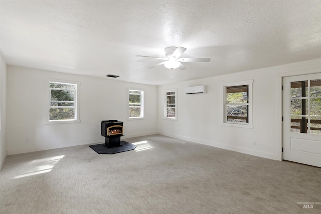 unfurnished living room with a wealth of natural light, a wood stove, a wall mounted air conditioner, and visible vents