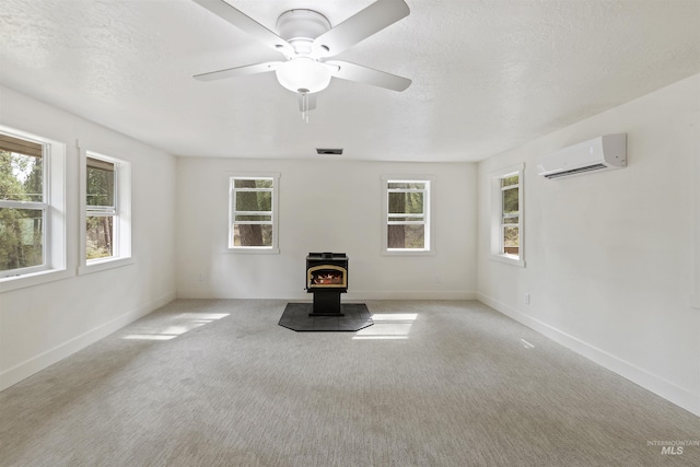 unfurnished living room with baseboards, a wood stove, a textured ceiling, carpet floors, and a wall mounted AC
