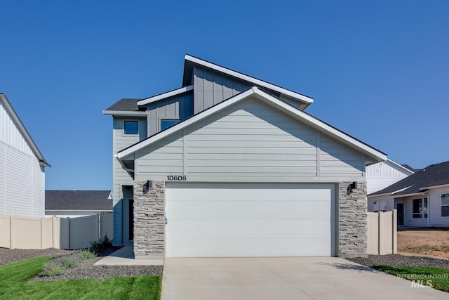 view of front of house with concrete driveway, stone siding, an attached garage, fence, and board and batten siding