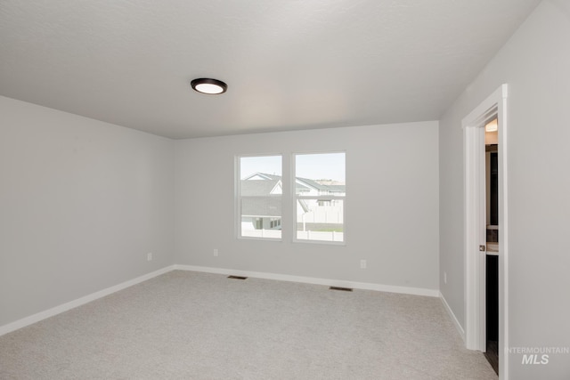 spare room featuring light carpet, visible vents, and baseboards