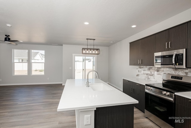 kitchen with stainless steel appliances, light countertops, open floor plan, a kitchen island with sink, and a sink