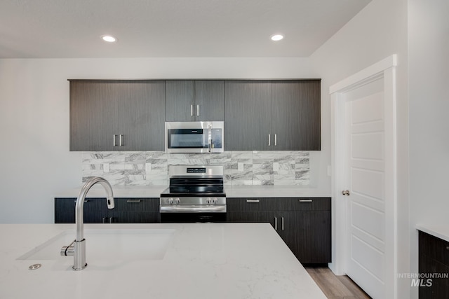 kitchen with tasteful backsplash, appliances with stainless steel finishes, light countertops, a sink, and recessed lighting