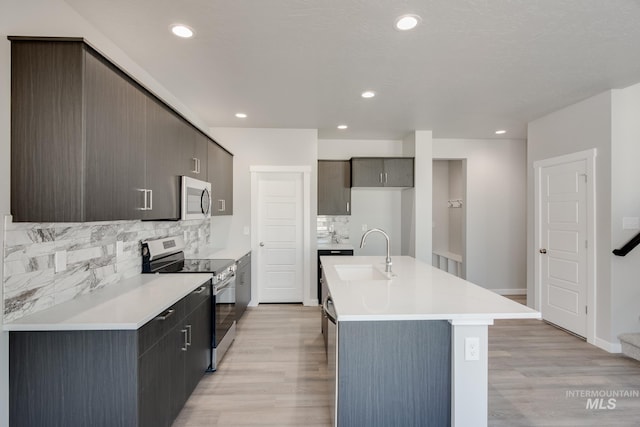 kitchen with stainless steel appliances, light countertops, a sink, and light wood-style flooring