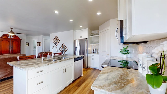 kitchen featuring a kitchen island with sink, light wood-style flooring, a sink, stainless steel appliances, and white cabinets