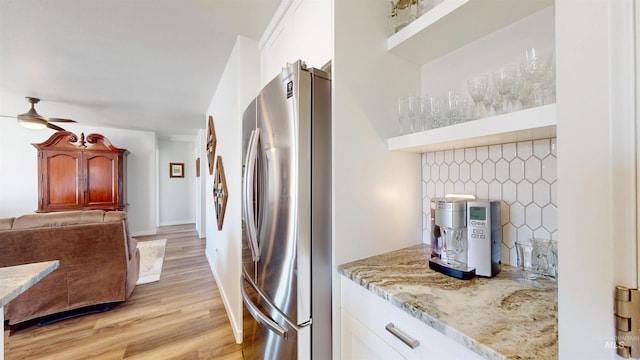 kitchen featuring light stone countertops, light wood-style flooring, freestanding refrigerator, ceiling fan, and backsplash