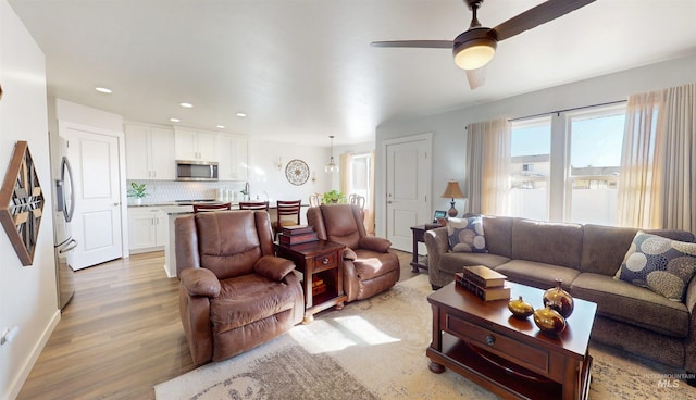 living area with baseboards, a healthy amount of sunlight, light wood-style flooring, and a ceiling fan