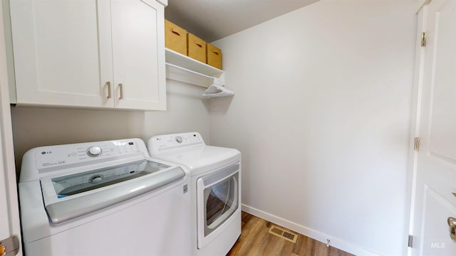 laundry area featuring baseboards, visible vents, washing machine and clothes dryer, light wood-style flooring, and cabinet space