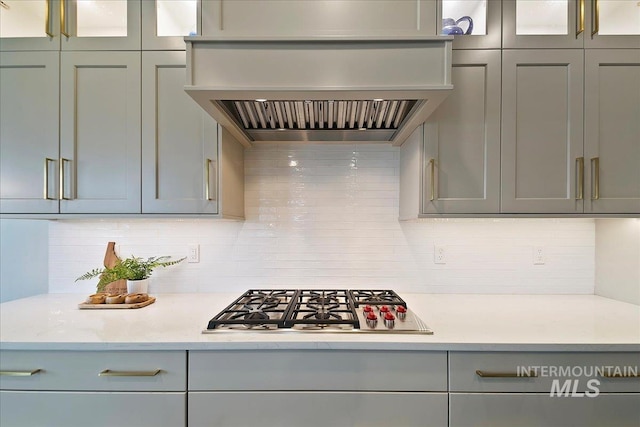 kitchen with custom exhaust hood, decorative backsplash, stainless steel gas cooktop, and light stone countertops