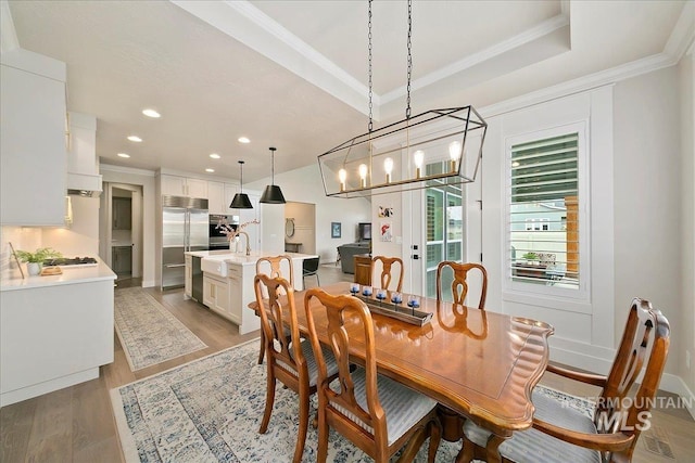 dining space with a raised ceiling, a chandelier, ornamental molding, and light hardwood / wood-style floors