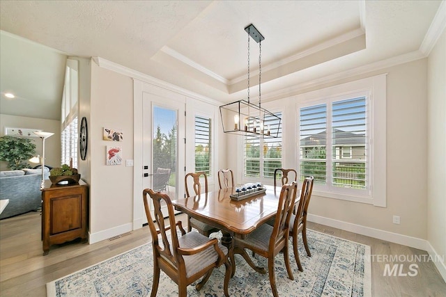 dining area with ornamental molding, a raised ceiling, light wood-type flooring, and a notable chandelier