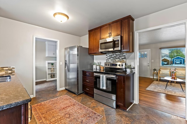 kitchen with a sink, dark countertops, tasteful backsplash, appliances with stainless steel finishes, and baseboards