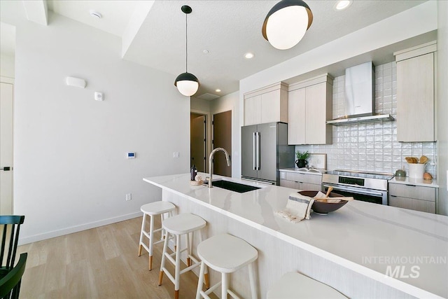 kitchen featuring wall chimney range hood, a sink, appliances with stainless steel finishes, a kitchen breakfast bar, and backsplash