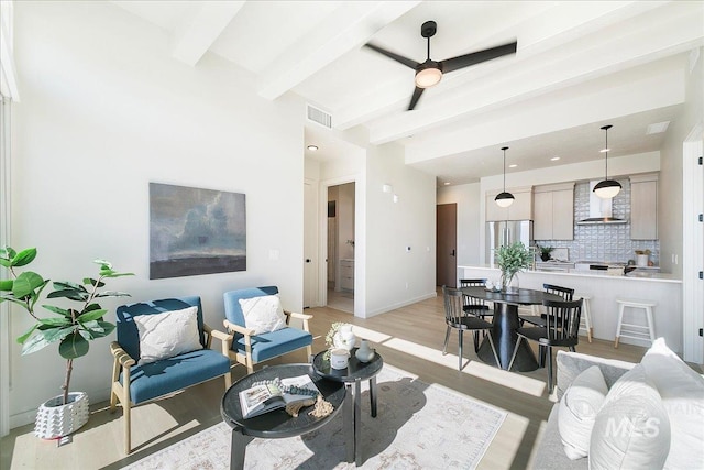 living area with a ceiling fan, visible vents, baseboards, light wood-style floors, and beamed ceiling