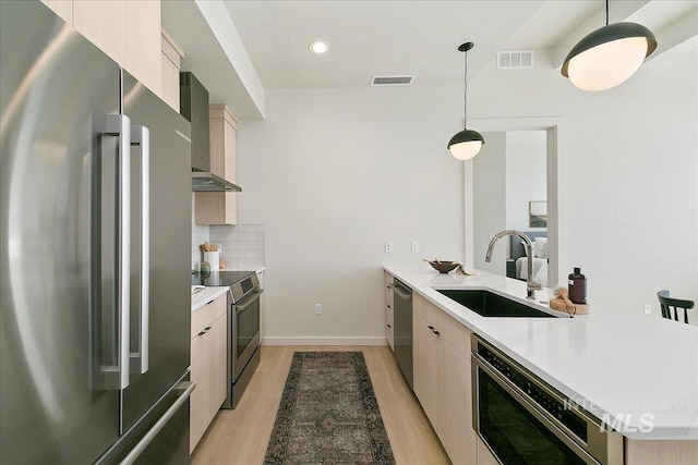 kitchen featuring visible vents, modern cabinets, a sink, appliances with stainless steel finishes, and wall chimney range hood