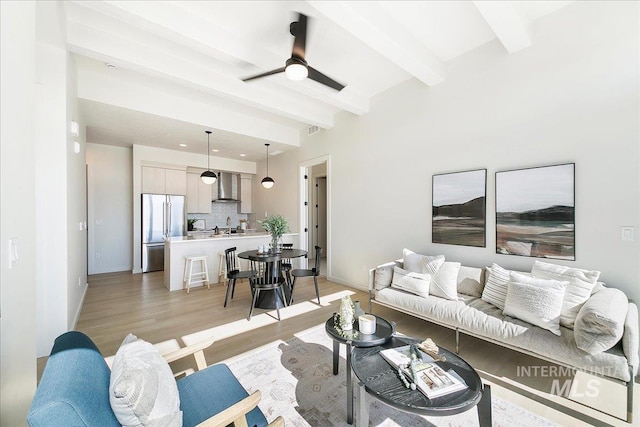 living room featuring baseboards, beam ceiling, light wood-style floors, and ceiling fan