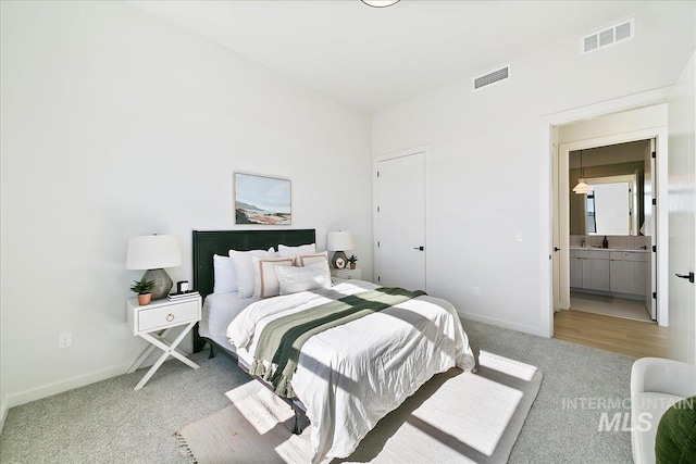 carpeted bedroom with ensuite bath, baseboards, and visible vents