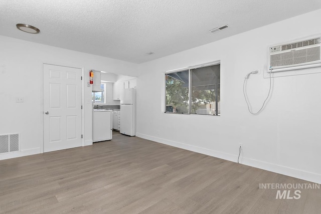 135 Davis Ave, Nampa, ID 83651 - unfurnished living room featuring separate washer and dryer, wood finished floors, a textured ceiling, baseboards, and a wall unit AC