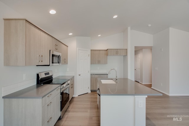 kitchen with light brown cabinets, stainless steel appliances, sink, a kitchen island with sink, and vaulted ceiling